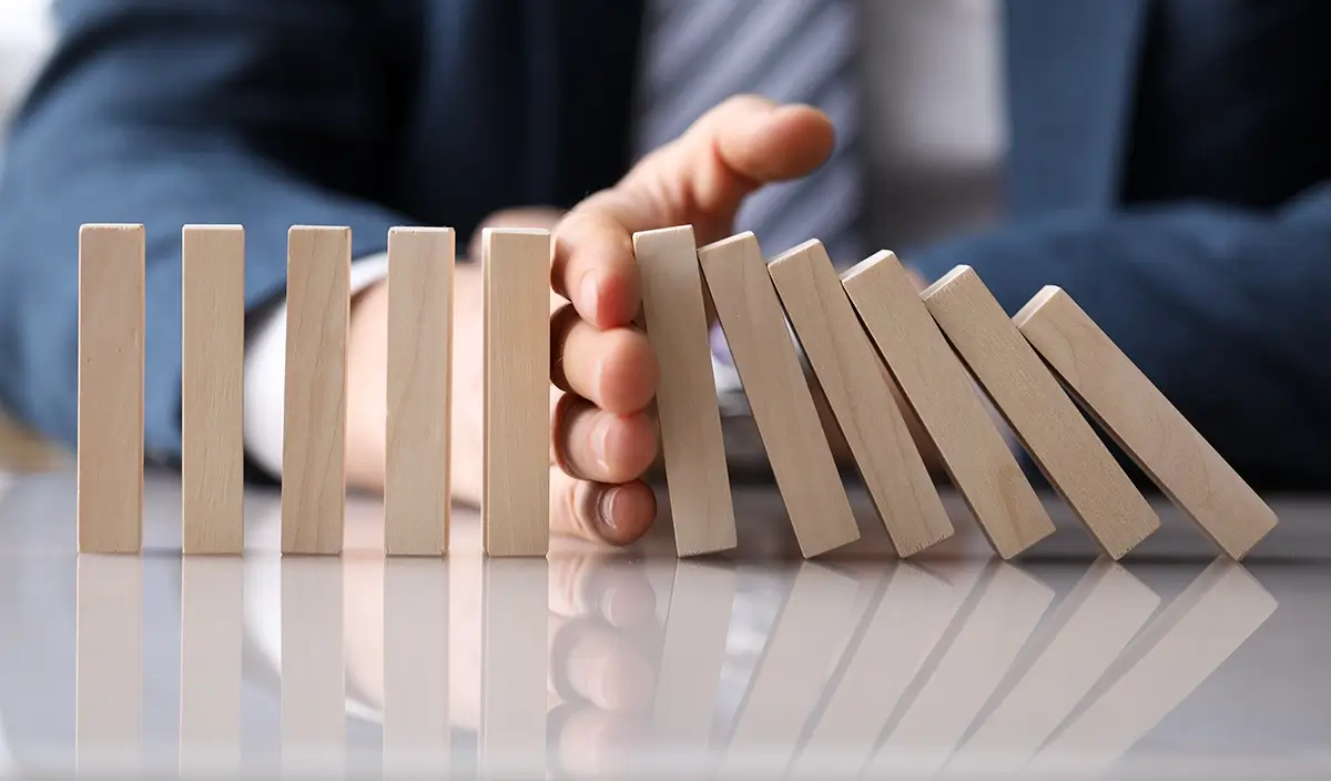 Person using hand to stop sequence of wooden blocks from falling, signifying a halt in a project